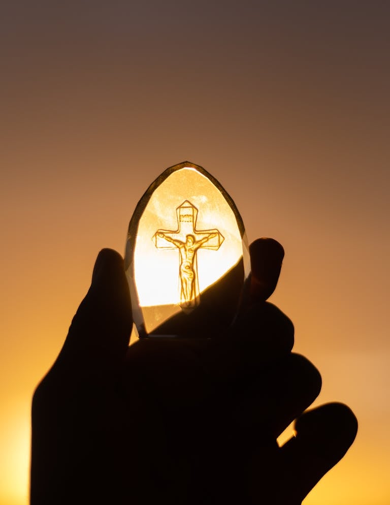 A silhouetted hand holds a crucifix against a vibrant sunset sky, symbolizing faith and spirituality.